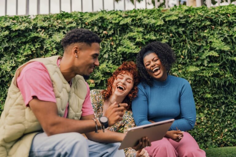 three gen z employees sitting outside and laughing in front of laptop