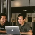 2 employees smiling in front of laptop and showing the role of purpose in employer branding