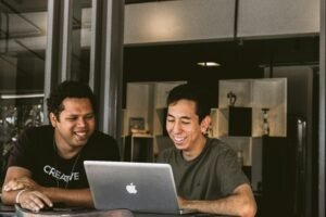 2 employees smiling in front of laptop and showing the role of purpose in employer branding