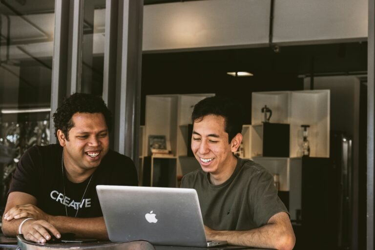 2 employees smiling in front of laptop and showing the role of purpose in employer branding