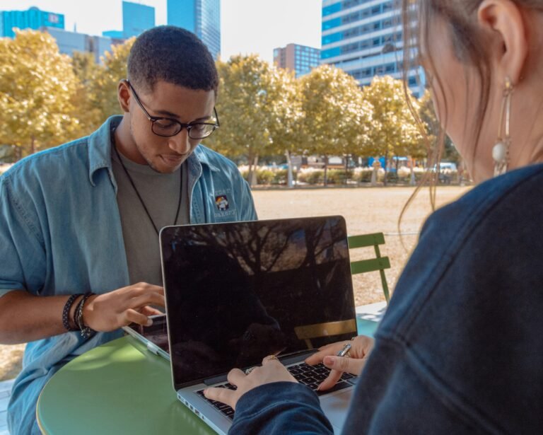 Two people working on their laptop on a table outside